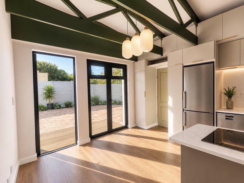 Modern open-plan kitchen and living area featuring exposed green beams, high-end cabinetry, stone countertops, and direct access to a private paved patio.