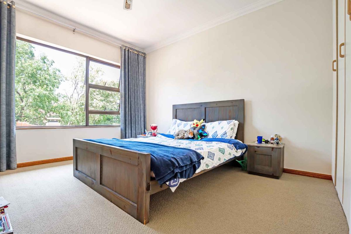 A well-lit bedroom featuring neutral carpeting, built-in wardrobe cabinetry, and a large window providing natural light and garden views.
