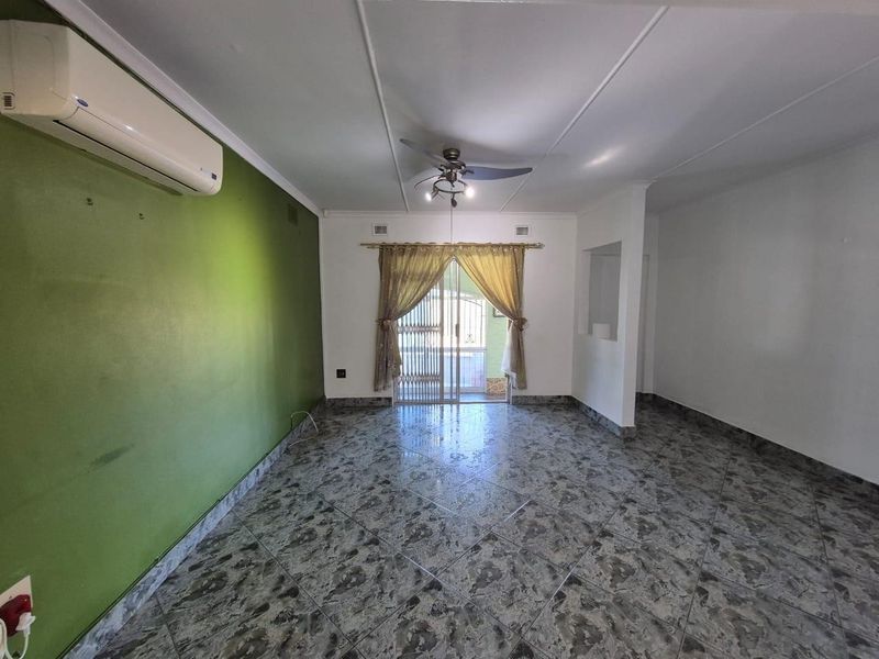Spacious living area featuring tiled flooring, a ceiling fan, and a wall-mounted air conditioning unit, with direct access to an outdoor space.