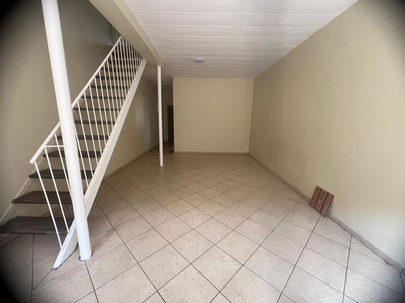 An empty, open-plan living area featuring neutral tiled flooring, a white staircase, and a support column, offering a blank canvas for interior design.