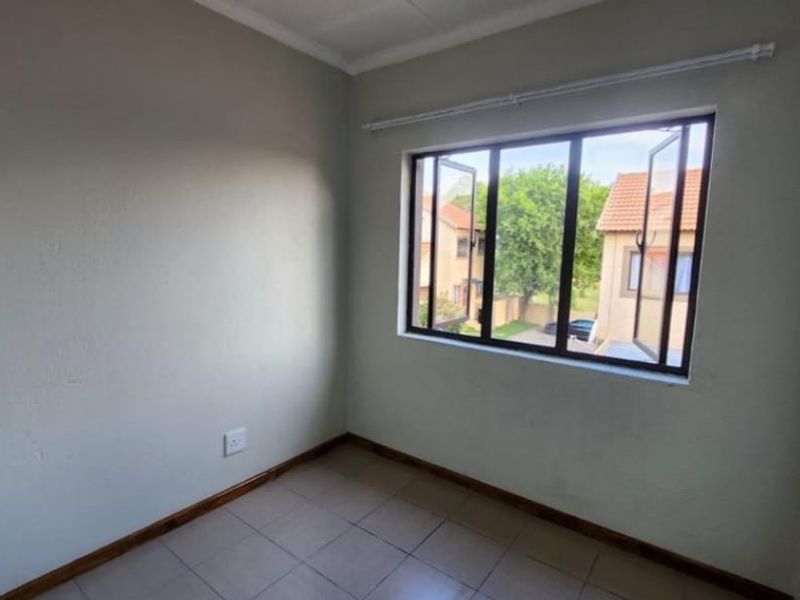 A clean, empty bedroom featuring tiled flooring, neutral walls, and a large casement window providing natural light and a view of the complex.