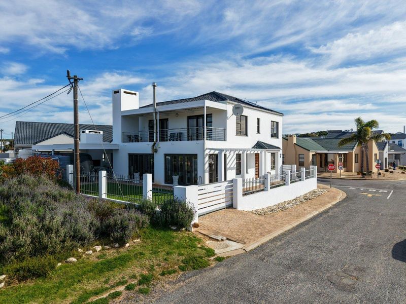 A well-maintained two-story residential property featuring a white facade, balcony, paved driveway, and secure perimeter fencing in a quiet street setting.