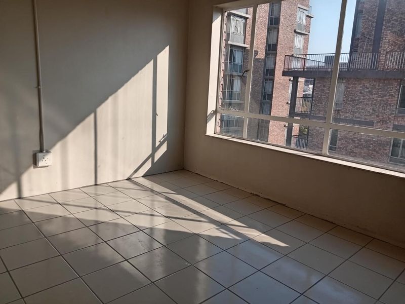 An empty bedroom featuring tiled flooring and a large window with natural light, providing a blank canvas for interior design.