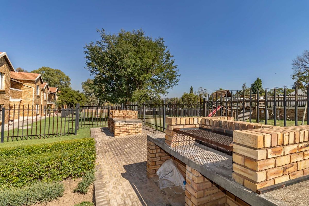 Outdoor communal area featuring brick braai facilities, paved patio space, and secure metal perimeter fencing within a well-maintained garden setting.