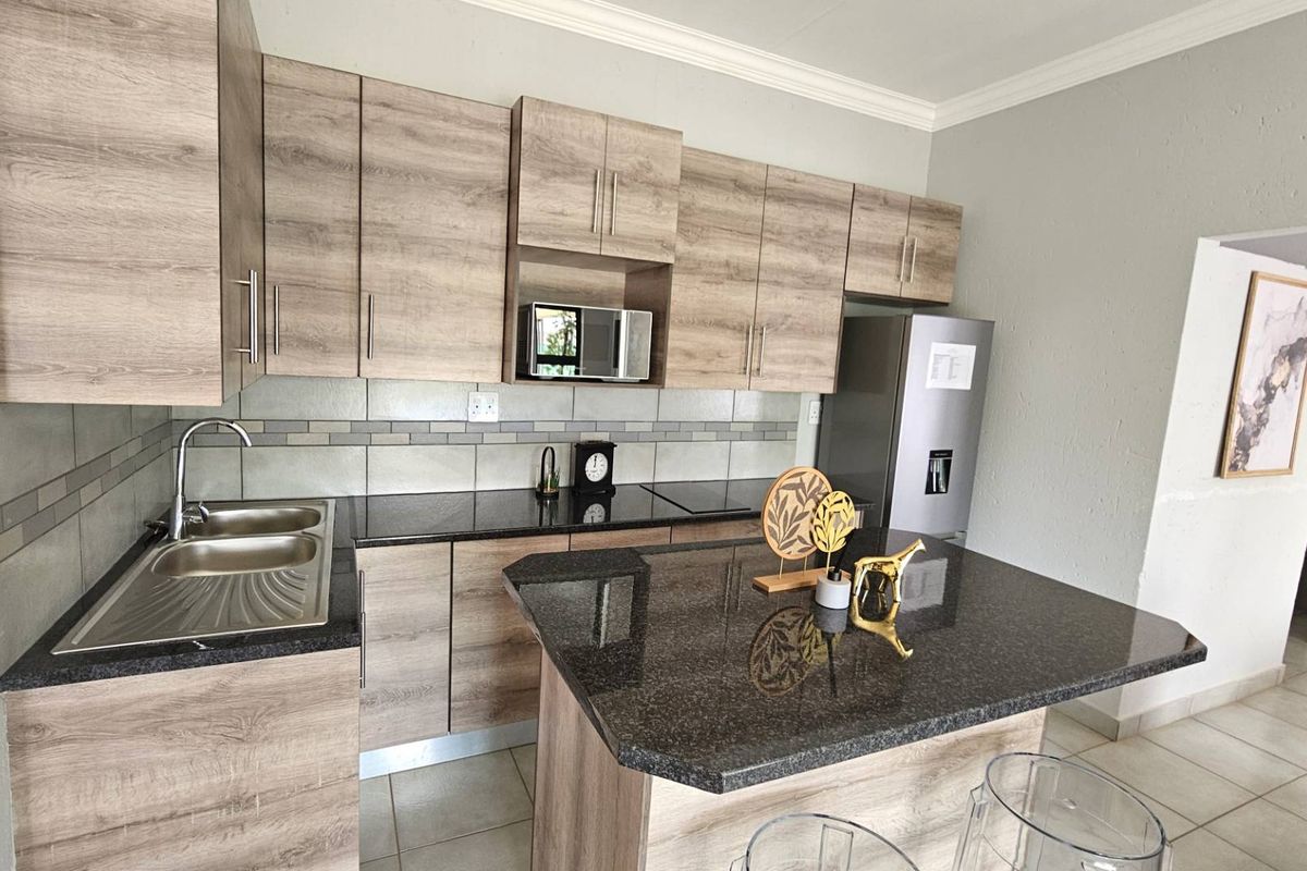 Modern kitchen featuring wood-grain cabinetry, granite countertops, a central island, and a double-basin stainless steel sink.