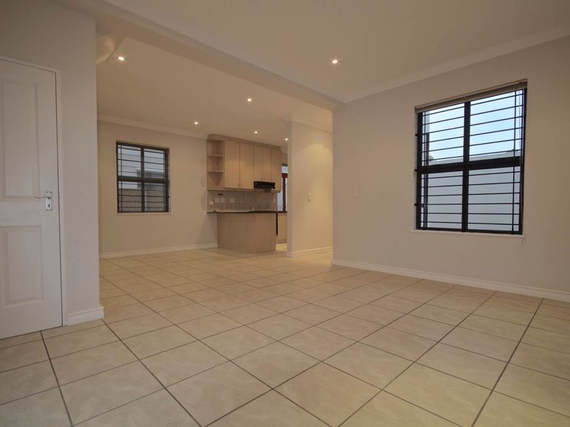 Spacious open-plan living area featuring neutral tiled flooring, recessed lighting, and a functional kitchen with built-in cabinetry and an extractor fan.
