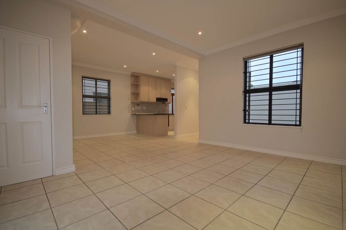 Spacious open-plan living area featuring neutral tiled flooring, recessed lighting, and a functional kitchen with built-in cabinetry and an extractor fan.