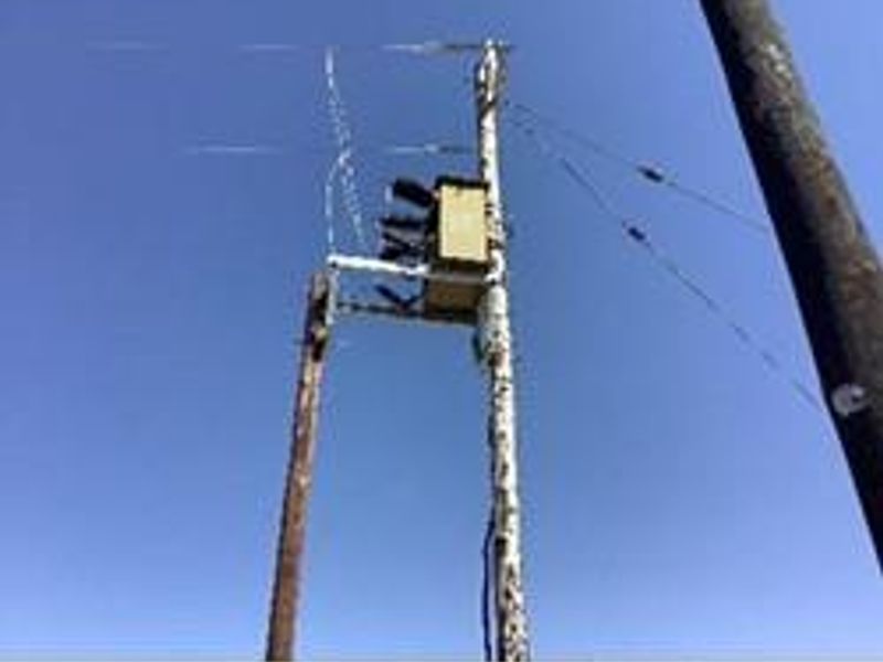An outdoor utility pole featuring an electrical transformer against a clear blue sky.