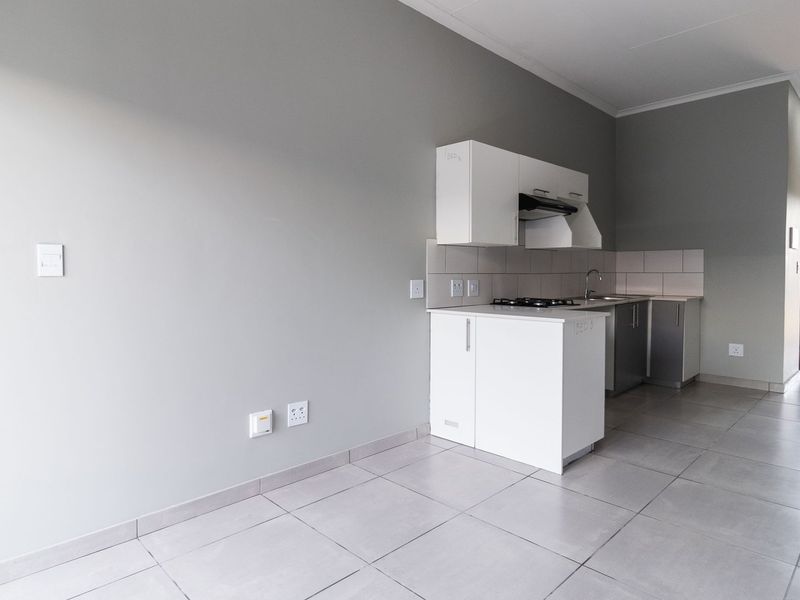 An open-plan living and kitchen area featuring neutral grey walls, tiled flooring, and a compact kitchen unit with built-in cabinetry and a gas hob.