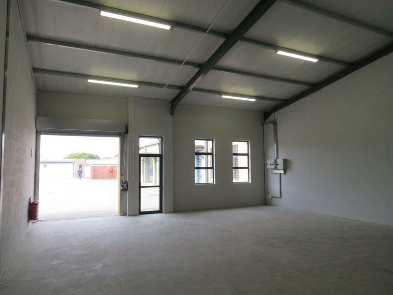 Spacious industrial utility space featuring concrete flooring, exposed steel roof trusses, fluorescent lighting, and a large roller shutter door for easy access.