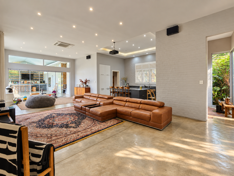 Spacious open-plan living area featuring polished concrete floors, an exposed brick wall, modern kitchen island, and seamless indoor-outdoor flow through large sliding glass doors.