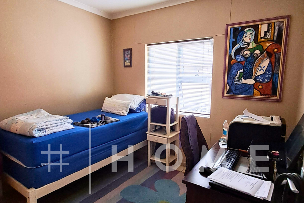 A compact bedroom featuring tiled flooring, a window with fitted blinds, and neutral wall finishes, suitable for a single bed and study area.