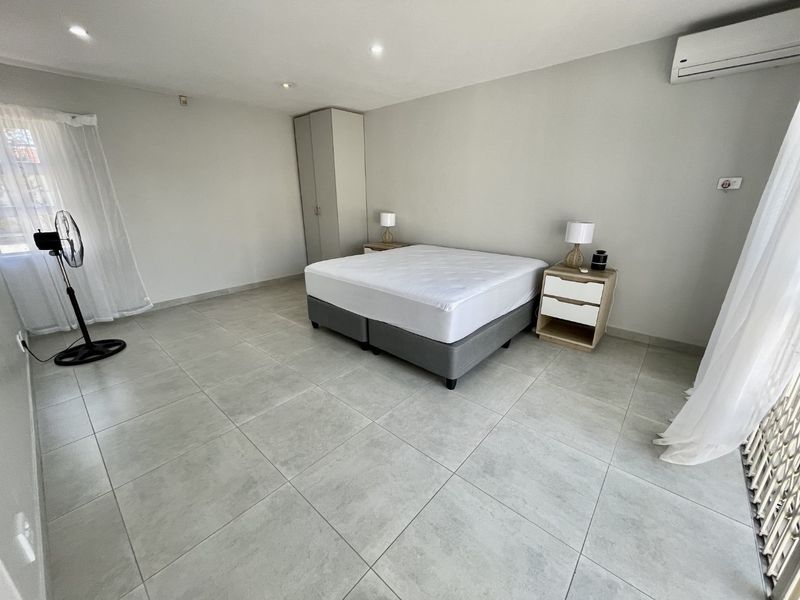 Spacious bedroom featuring neutral tiled flooring, built-in wardrobe, and a wall-mounted air conditioning unit.