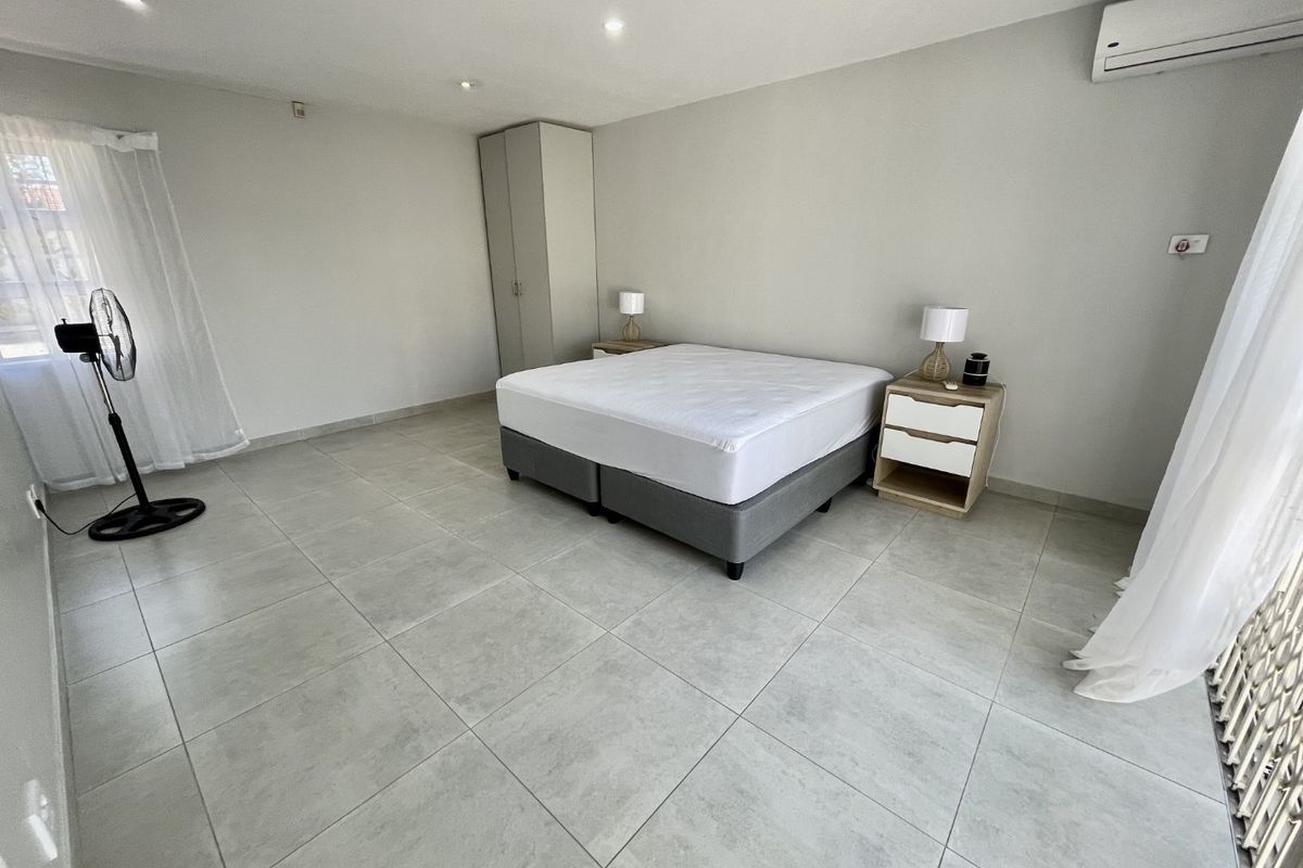 Spacious bedroom featuring neutral tiled flooring, built-in wardrobe, and a wall-mounted air conditioning unit.