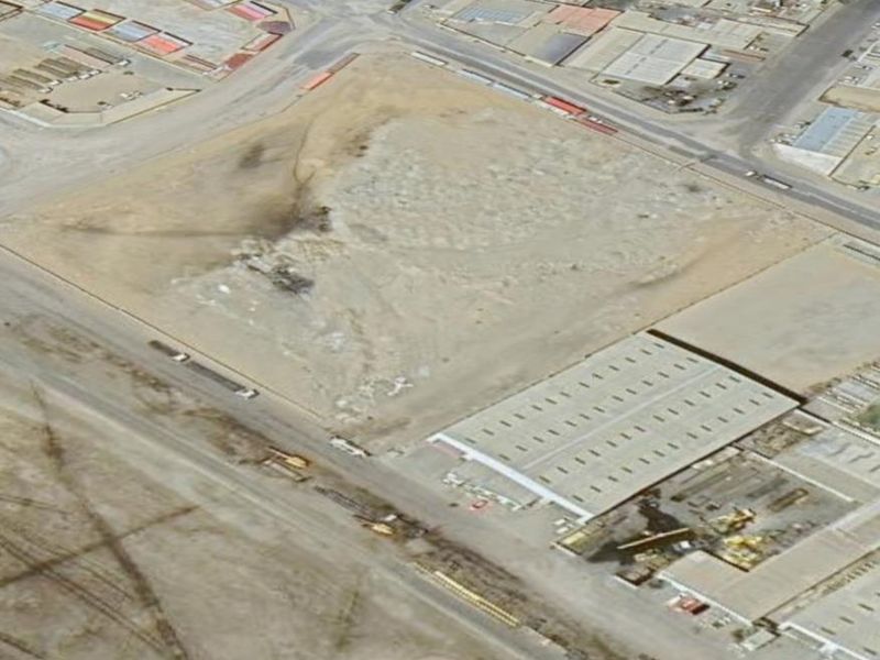 Aerial view of an industrial site featuring a warehouse structure and surrounding vacant land with established road access.