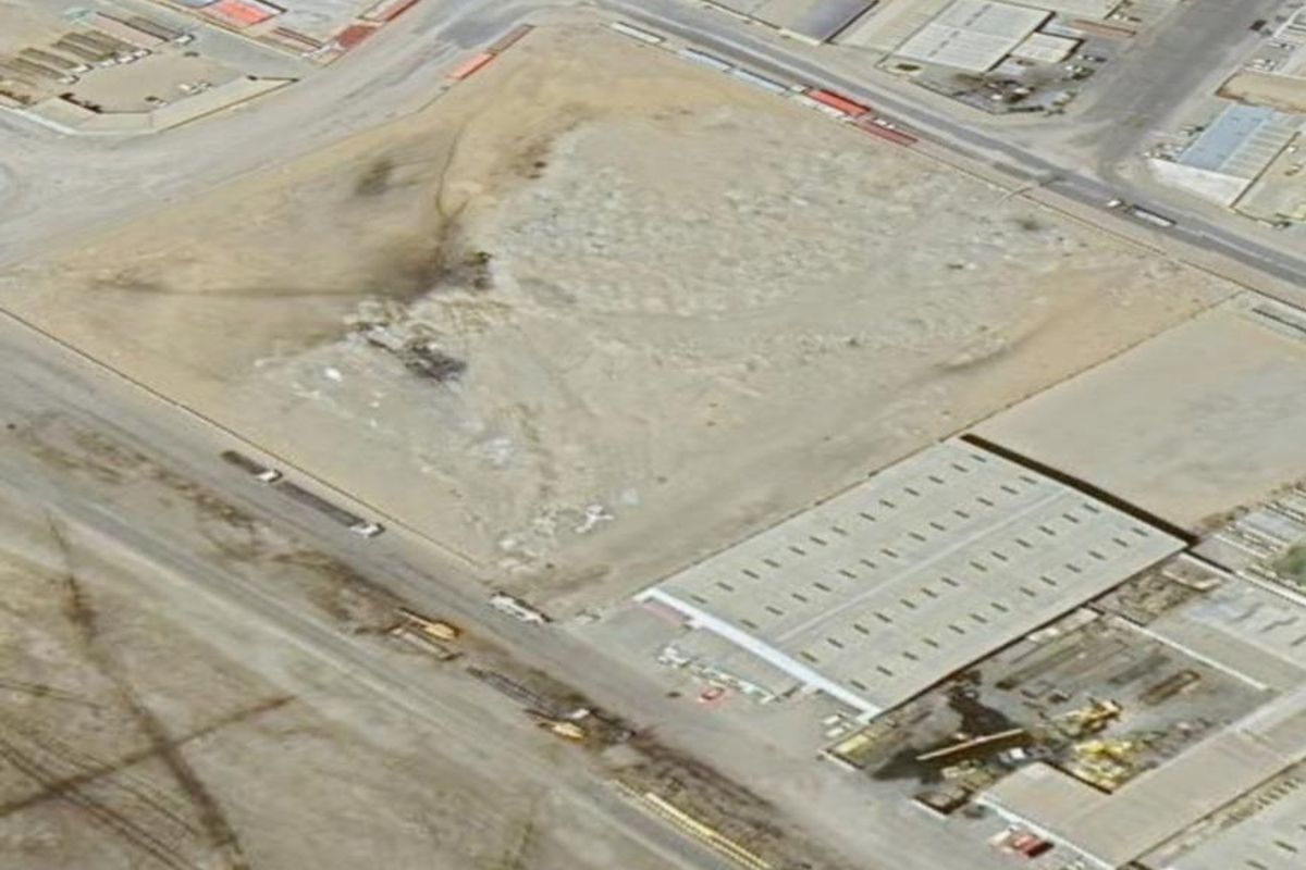 Aerial view of an industrial site featuring a warehouse structure and surrounding vacant land with established road access.
