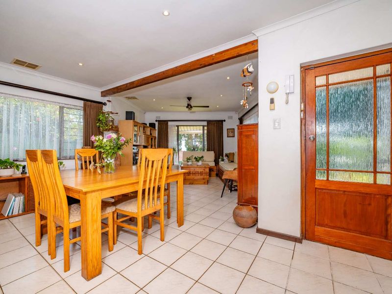 Open plan dining and living area featuring tiled flooring, an exposed timber beam, and a classic timber entrance door with glass panels.
