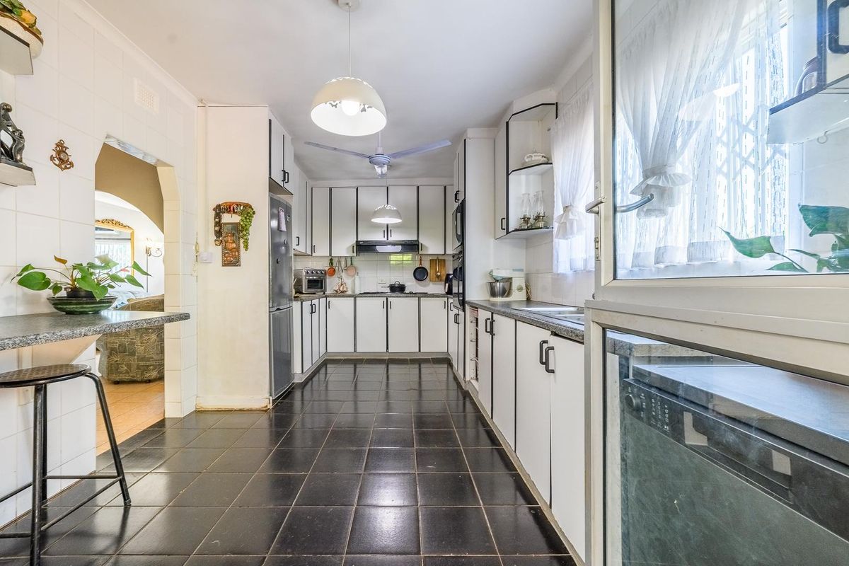 A functional kitchen featuring white cabinetry, dark tiled flooring, a breakfast bar, and built-in appliances, offering a practical layout with potential for modern updates.