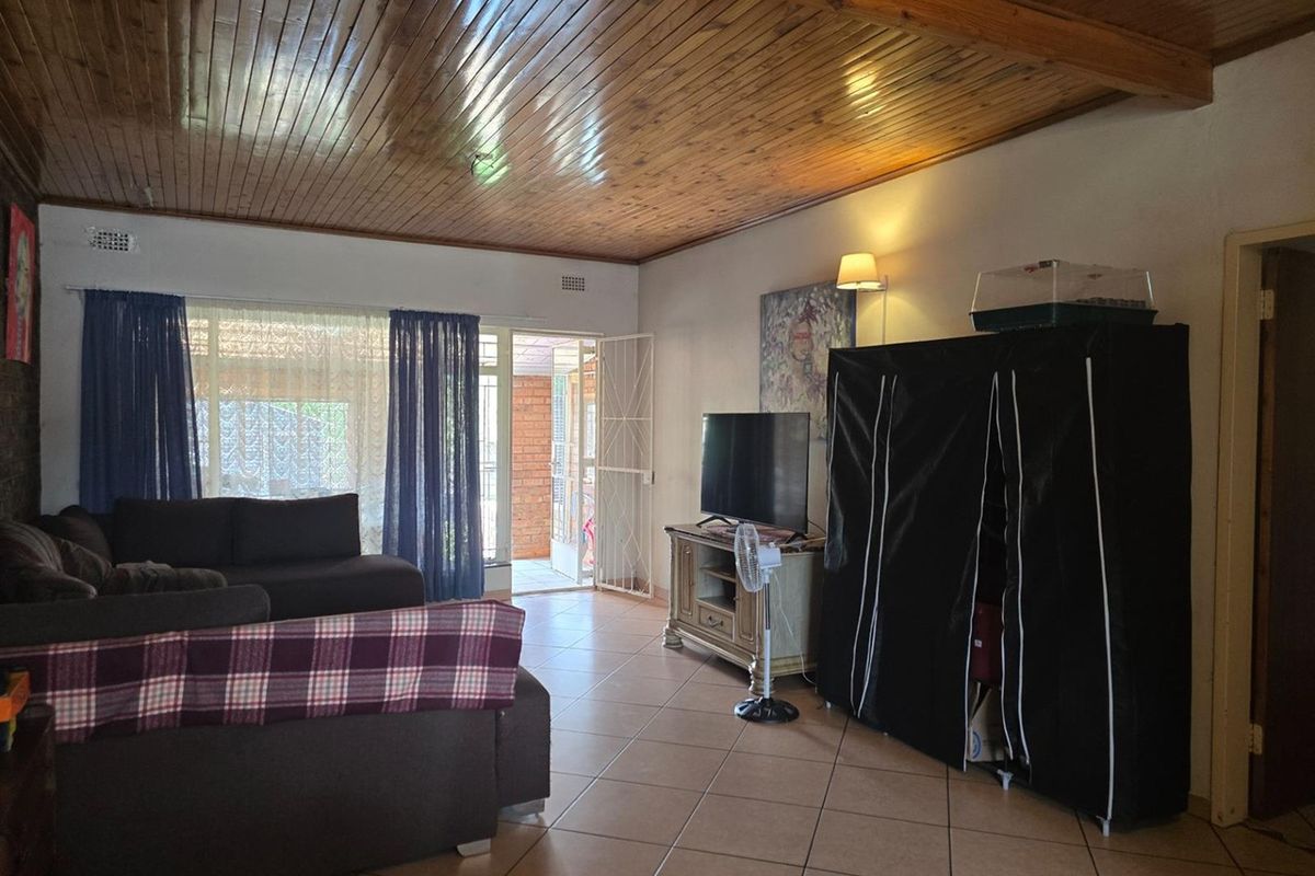 Spacious living room featuring ceramic floor tiles and a distinctive timber tongue and groove ceiling, with direct access to an outdoor patio area.