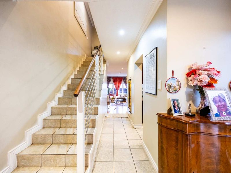 A bright hallway featuring tiled flooring and a staircase with a metal balustrade, leading towards the living area.