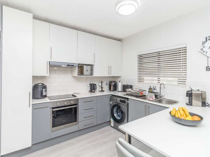 Modern kitchen featuring white and grey cabinetry, subway tile backsplash, integrated appliances, and a breakfast bar area with neutral laminate flooring.