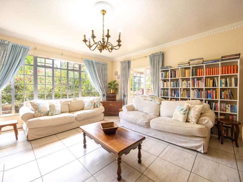 A bright living room featuring ceramic tile flooring, crown molding, a decorative ceiling rose, and large steel-framed windows overlooking the garden.