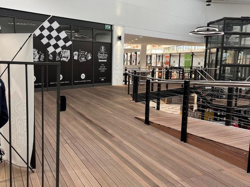 Modern retail mezzanine level featuring timber decking, metal balustrades, and exposed industrial-style ceiling ducting with natural light from overhead skylights.