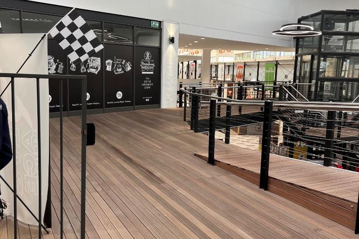 Modern retail mezzanine level featuring timber decking, metal balustrades, and exposed industrial-style ceiling ducting with natural light from overhead skylights.
