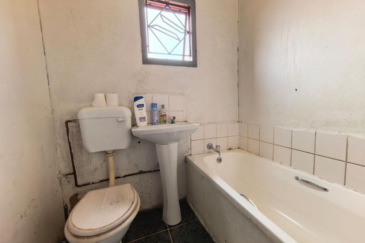 A dated bathroom featuring a pedestal basin, standard bathtub, and toilet, requiring significant cosmetic updates and maintenance to the wall finishes and fixtures.