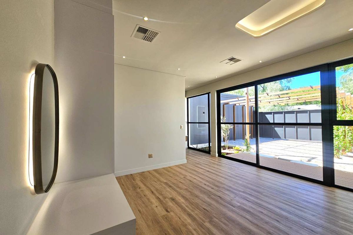 A bright, modern living area featuring timber-look flooring, recessed ceiling lighting, and large sliding glass doors that open onto a paved outdoor patio space.