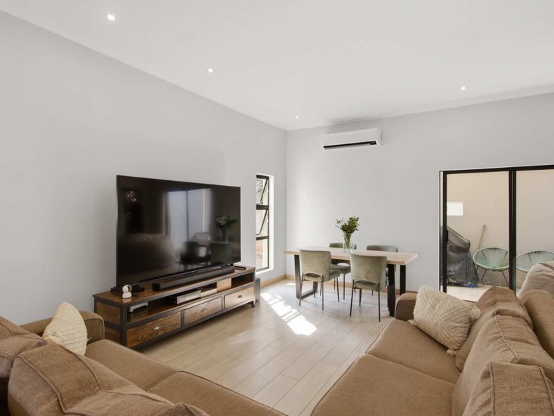 Modern open-plan living and dining area featuring neutral tiled flooring, recessed lighting, and a wall-mounted air conditioning unit with access to an outdoor space.