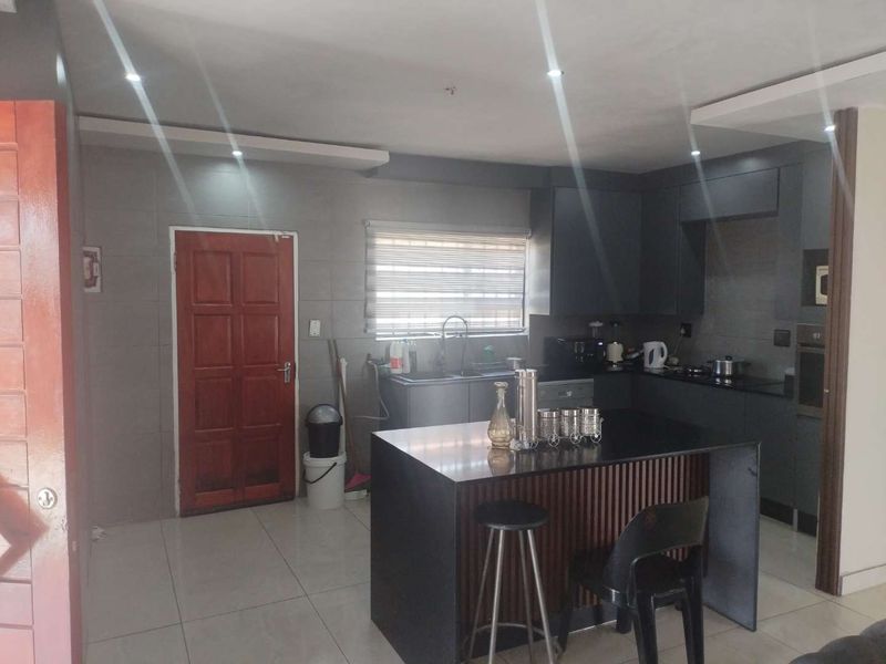 Modern kitchen featuring dark cabinetry, a central island with stone countertops, integrated oven, and tiled flooring with recessed lighting.