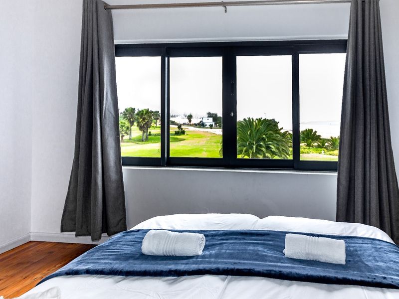 A bright bedroom featuring polished hardwood flooring and a large sliding window that offers scenic views of the surrounding landscape.
