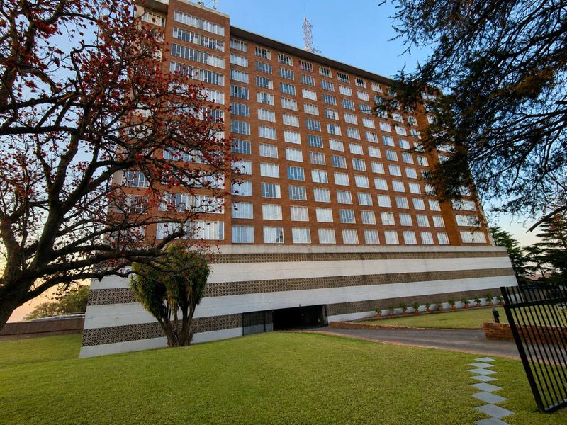 A wide-angle view of a multi-story brick apartment building featuring a landscaped lawn and an underground parking entrance.