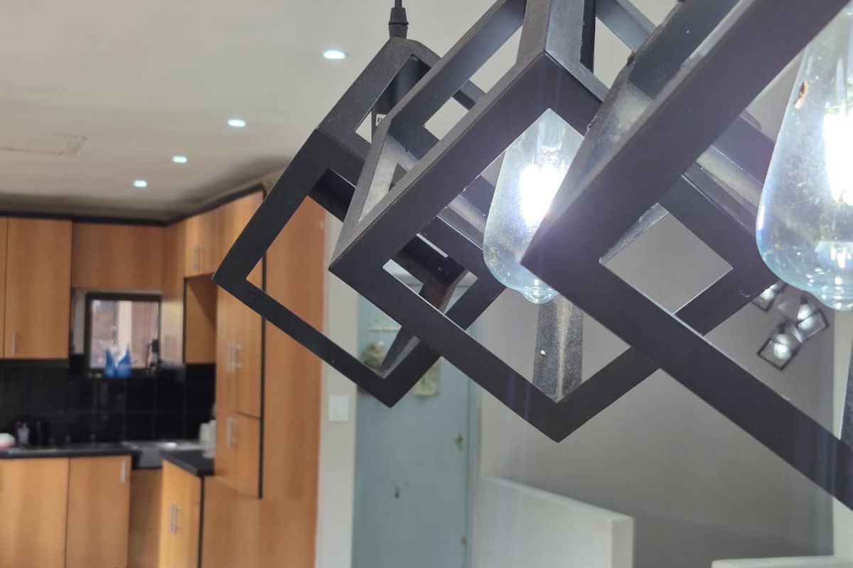A close-up view of modern geometric pendant lighting in a kitchen featuring wooden cabinetry and dark countertops.