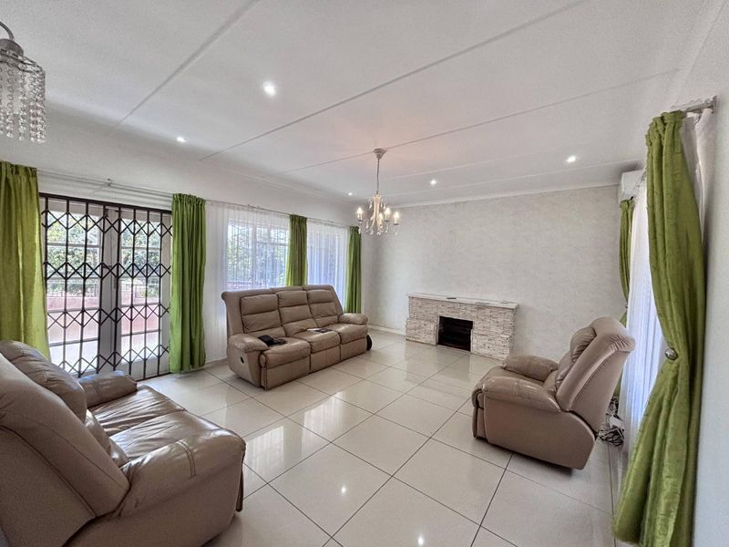 Spacious living room featuring large format floor tiles, a stone-clad fireplace, recessed lighting, and direct access to the exterior through a security-gated sliding door.