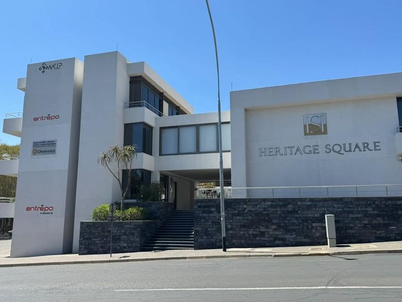Modern multi-story office building facade featuring stone cladding, glass windows, and prominent signage for Heritage Square.