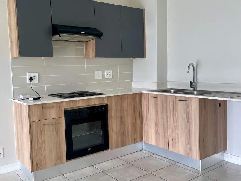 Modern kitchen featuring wood-grain cabinetry, stone-look countertops, built-in oven, electric hob, extractor fan, and a stainless steel double sink with tiled flooring.