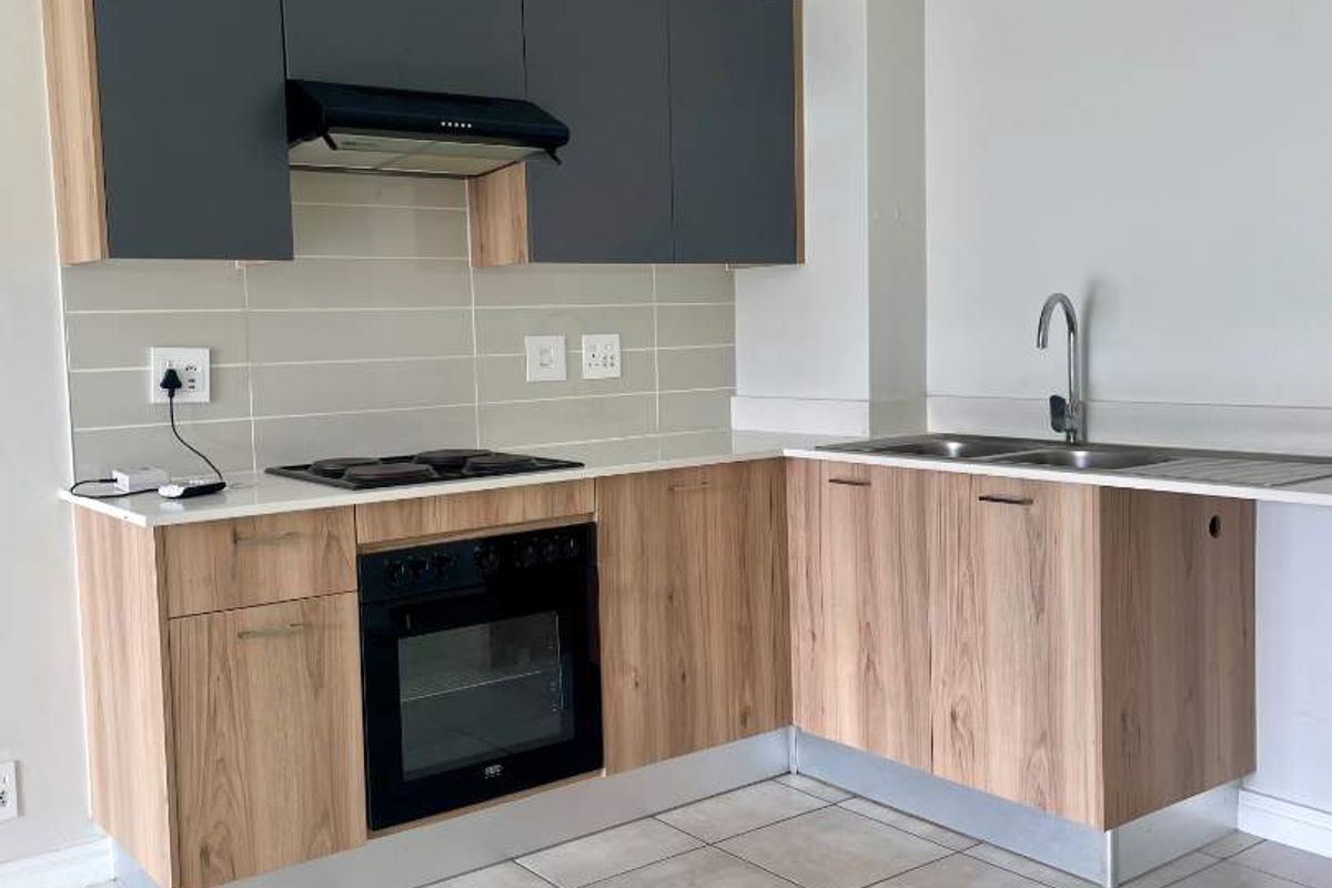 Modern kitchen featuring wood-grain cabinetry, stone-look countertops, built-in oven, electric hob, extractor fan, and a stainless steel double sink with tiled flooring.