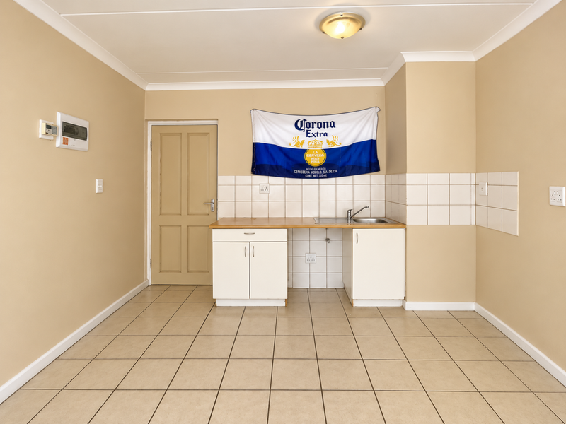 A functional, empty kitchen area featuring tiled flooring, a built-in sink unit with cabinetry, and a tiled backsplash.