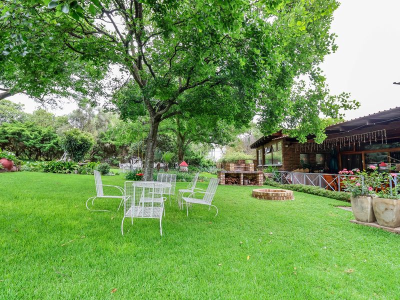 A lush, well-maintained garden featuring a brick built-in braai, a fire pit, and a covered patio area attached to the main dwelling.