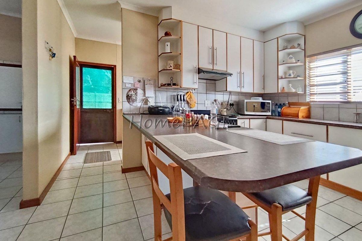 A functional kitchen featuring built-in cabinetry, a breakfast bar, tiled flooring, and an integrated extractor fan, with direct access to an exterior door.