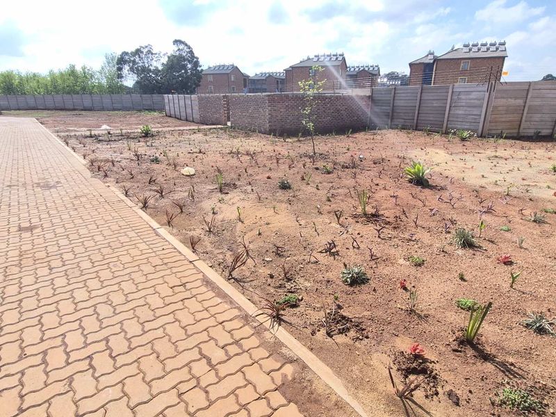 An outdoor garden area featuring a paved walkway, precast concrete boundary walls, and electric fencing, currently awaiting further landscaping and development.