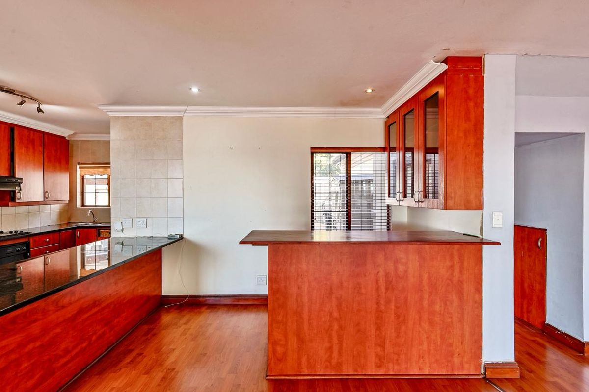 A spacious kitchen featuring wooden cabinetry, granite countertops, a breakfast bar, and laminate flooring, offering a functional layout ready for modern updates.