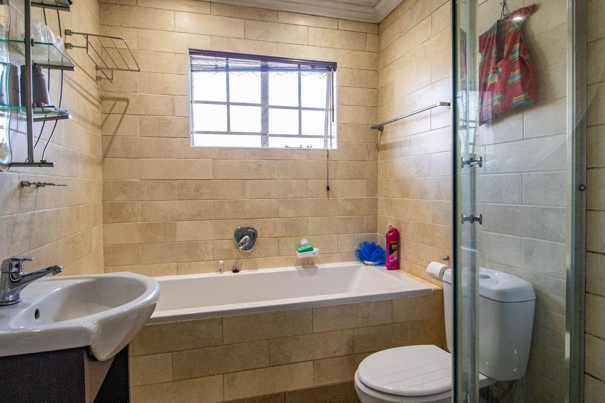 A functional bathroom featuring a built-in bathtub, separate glass-enclosed shower, pedestal basin, and tiled wall finishes.