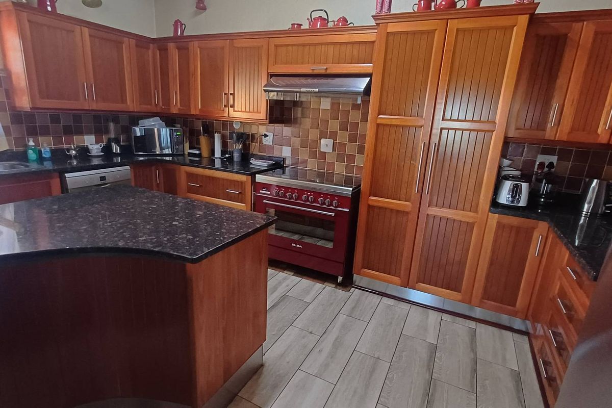 A traditional kitchen featuring warm-toned wooden cabinetry, dark granite countertops, a tiled backsplash, and a freestanding red oven with an integrated extractor fan.