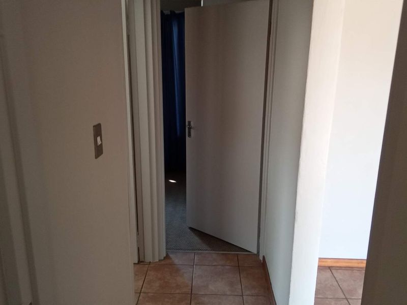 A view of a simple interior hallway with tiled flooring and access to adjacent rooms.