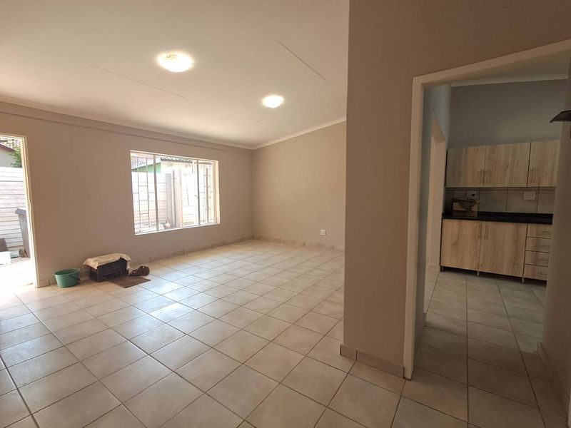 Spacious open-plan living area featuring neutral tiled flooring and recessed lighting, with an adjacent kitchen area showcasing modern wood-finish cabinetry.