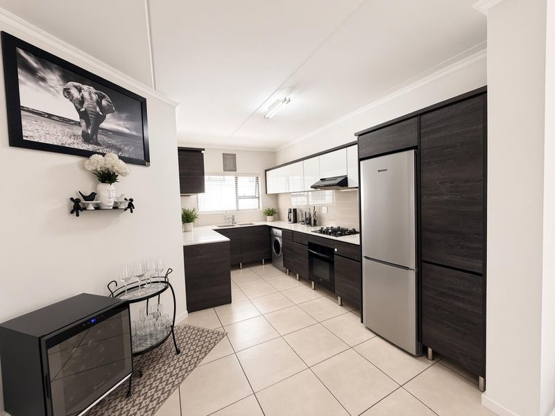 Modern kitchen featuring dark wood cabinetry, light countertops, gas hob, built-in oven, extractor fan, and tiled flooring in an open-plan layout.