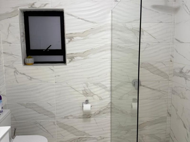 Modern bathroom featuring a walk-in shower with a rainfall shower head, marble-look wall and floor tiles, and a contemporary toilet.